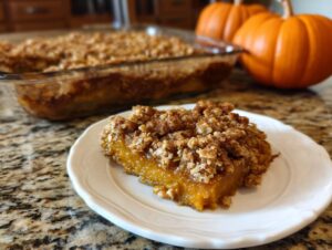 A slice of delicious pumpkin oatmeal dump cake on a white plate, with the rest of the cake in a glass dish in the background.