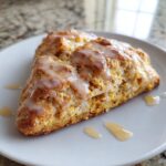 Close-up of two tender pumpkin scones drizzled with a sweet glaze on a white plate.