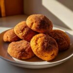 A stack of freshly baked pumpkin snickerdoodle cookies, coated in cinnamon sugar, on a white plate.