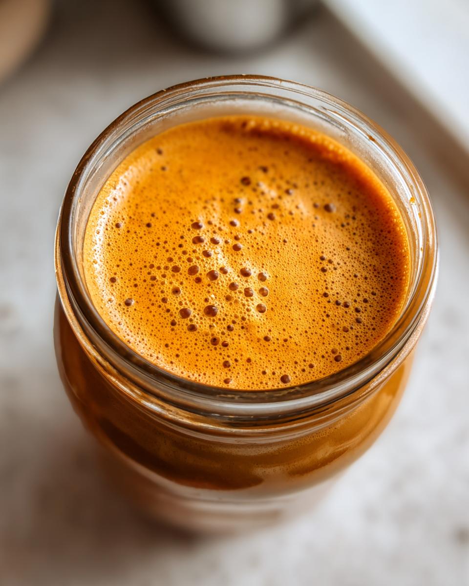 Close-up of frothy, orange pumpkin spice coffee creamer in a glass jar.