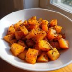 Close-up of perfectly roasted butternut squash cubes seasoned with herbs in a white bowl.
