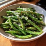 A bowl of freshly roasted parmesan green beans, glistening and topped with grated parmesan cheese.