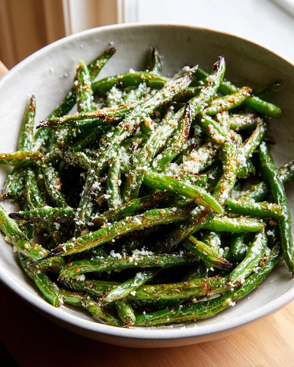 A close-up of a bowl filled with perfectly roasted parmesan green beans, lightly sprinkled with grated cheese.