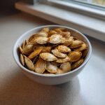 A white bowl filled with seasoned roasted pumpkin seeds, ready to be enjoyed.