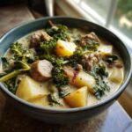A close-up of a bowl of slow cooker zuppa toscana, filled with sausage, potatoes, and kale in a creamy broth.