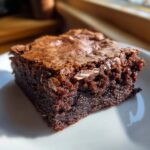 A close-up of a fudgy sourdough discard brownie slice on a white plate, showing its rich chocolate texture.