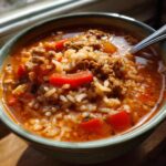 A close-up of a bowl of stuffed pepper soup, featuring ground beef, red bell peppers, and rice in a rich tomato broth.