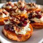 Close-up of festive sweet potato rounds topped with creamy goat cheese, dried cranberries, and toasted pecans.