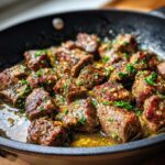 Close-up of sizzling Texas Roadhouse steak bites in a cast iron skillet, seasoned with herbs and garlic.