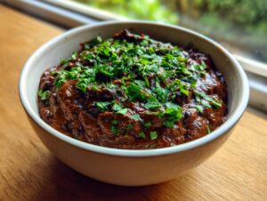 A close-up of rich, dark brown black bean dip in a white bowl, garnished generously with fresh chopped cilantro.