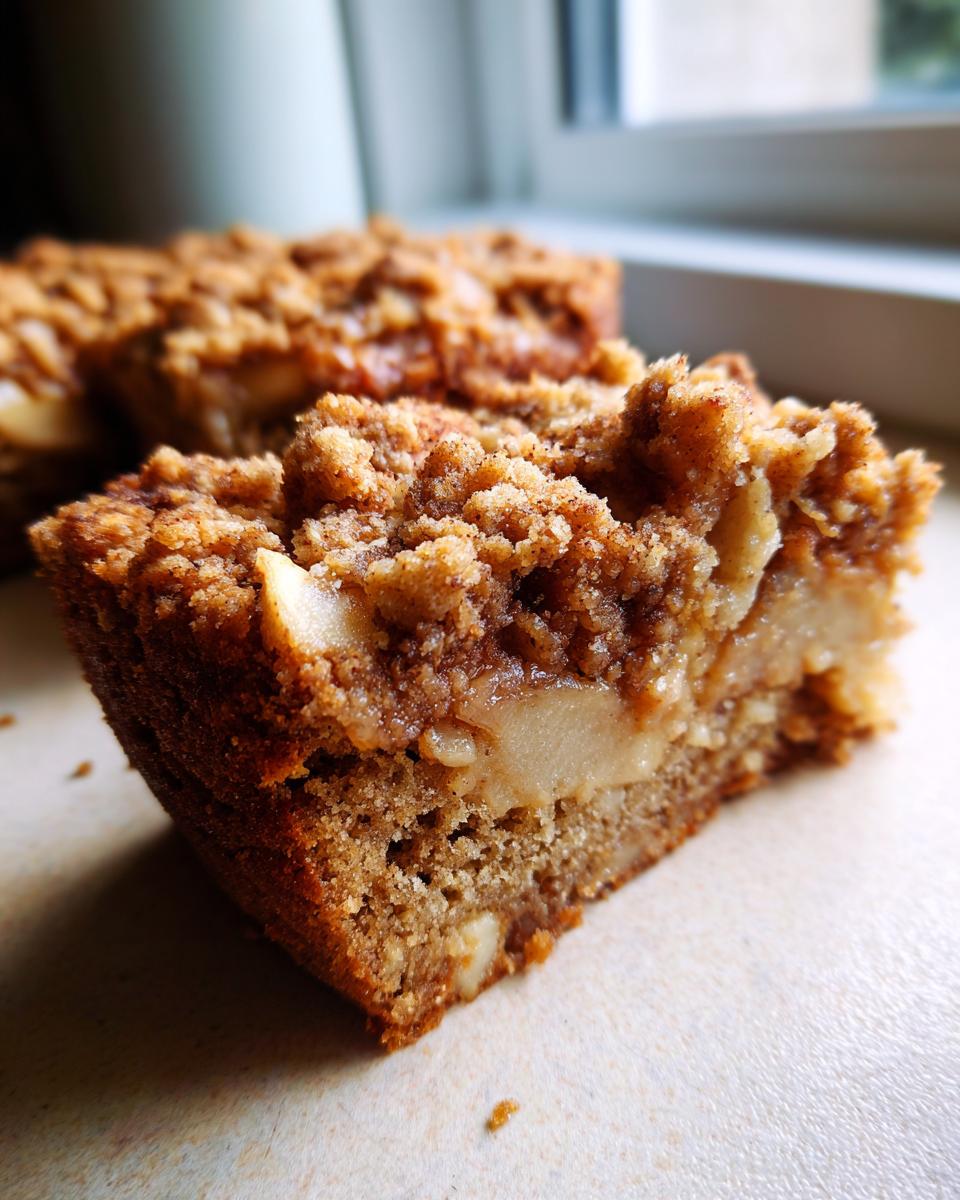 Close-up of a moist slice of apple crumb cake, showing tender apple pieces and a crunchy crumb topping.