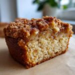 A close-up of a moist slice of apple crumb cake, showcasing the tender cake, chunks of apple, and sweet crumb topping.