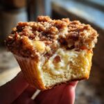 A close-up of an Apple Crumble Cheesecake Bun, showing its crumb topping and a gooey, creamy cheesecake filling.