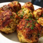 Close-up of golden brown baked chicken ricotta meatballs, sprinkled with fresh parsley, on a white plate.