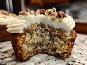 Close-up of a delicious banana cinnamon pecan cupcake with cream cheese frosting and chopped pecans.