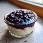 A close-up of a glass ramekin filled with creamy Blueberry Vanilla Bean Panna Cotta topped with a rich blueberry compote.