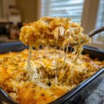 A spoonful of cheesy chicken and rice lifted from a baking dish, showing long, stretchy cheese pulls.