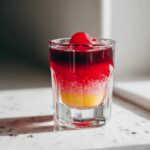 A close-up of layered cherry shots in a glass, topped with a cherry.