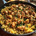 A close-up of chicken with buttered noodles in a skillet, garnished with fresh parsley.