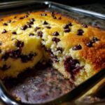 A close-up of a freshly baked chocolate cherry dump cake in a glass baking dish, studded with chocolate chips and bursting with cherries.