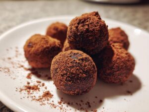 A close-up of several rich chocolate ricotta truffles dusted with cocoa powder on a white plate.
