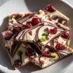 Close-up of swirled dark and white chocolate Christmas bark topped with dried cranberries, crushed candy canes, and pistachios.