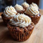 Close-up of delicious Christmas pudding cupcakes topped with swirls of creamy frosting on a wooden board.