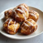 A close-up of a pile of golden brown cinnamon roll bites, generously drizzled with white icing.