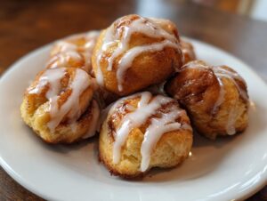 A close-up of fluffy cinnamon roll bites drizzled with white glaze on a white plate.