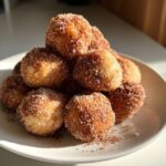 A close-up pile of freshly made cinnamon sugar donut holes on a white plate.