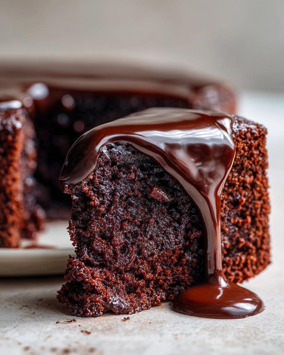 A close-up of a moist slice of easy chocolate cake with rich chocolate ganache being drizzled over it.