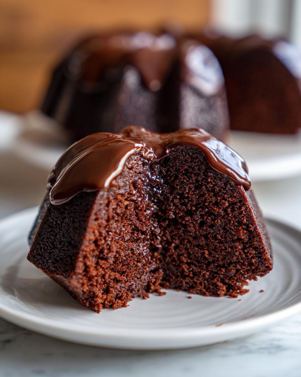 A moist slice of easy chocolate cake, topped with rich chocolate glaze, on a white plate.