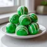 A pile of vibrant green Little Debbie cake balls, drizzled with white icing and sprinkled with white sugar.