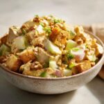 A close-up of a bowl of Honey Mustard Chicken Salad, featuring chunks of chicken, diced apples, croutons, and walnuts.