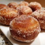 A close-up of several freshly made hot buttered mini donuts, generously coated in sparkling sugar.