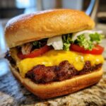 A close-up of a perfectly cooked juicy burger with melted cheddar cheese, fresh lettuce, tomato, and onion on a toasted bun.