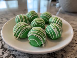 A plate of green Little Debbie cake balls decorated with white chocolate drizzle and green sprinkles.
