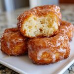 Close-up of fluffy maple donut bars, one broken in half to show the airy interior, all coated in a sweet glaze.