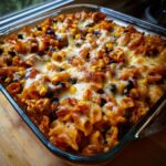 Close-up of a bubbling Mexican chicken pasta casserole with melted cheese, black beans, and corn.