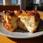 A close-up of a slice of old-fashioned bread pudding, with a golden-brown caramelized topping and a fluffy interior.