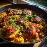 A close-up of oven baked chicken and rice in a cast iron skillet, garnished with fresh parsley.