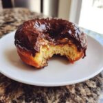 A bite taken out of a chocolate-glazed peanut butter cup stuffed donut, revealing the soft interior and gooey filling.