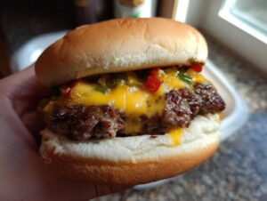 A close-up of a perfectly juicy burger with melted cheese and chopped peppers, held in a hand.