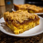 A close-up of a slice of pumpkin dump cake on a white plate, showcasing the crumb topping and pumpkin filling.