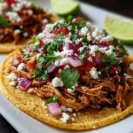 Close-up of a rotisserie chicken tostada topped with shredded chicken, salsa, cilantro, red onion, and crumbled cheese.