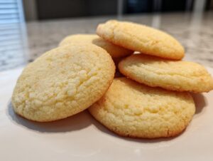 A close-up of a stack of golden-brown, soft sugar cookies on a white plate.