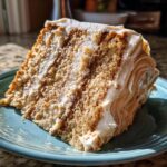 A close-up view of a thick slice of amazing spice cake layered with creamy frosting, sitting on a teal plate.