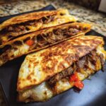 Close-up of golden-brown steak and cheese quesadilla slices, filled with shredded steak and melted cheese.
