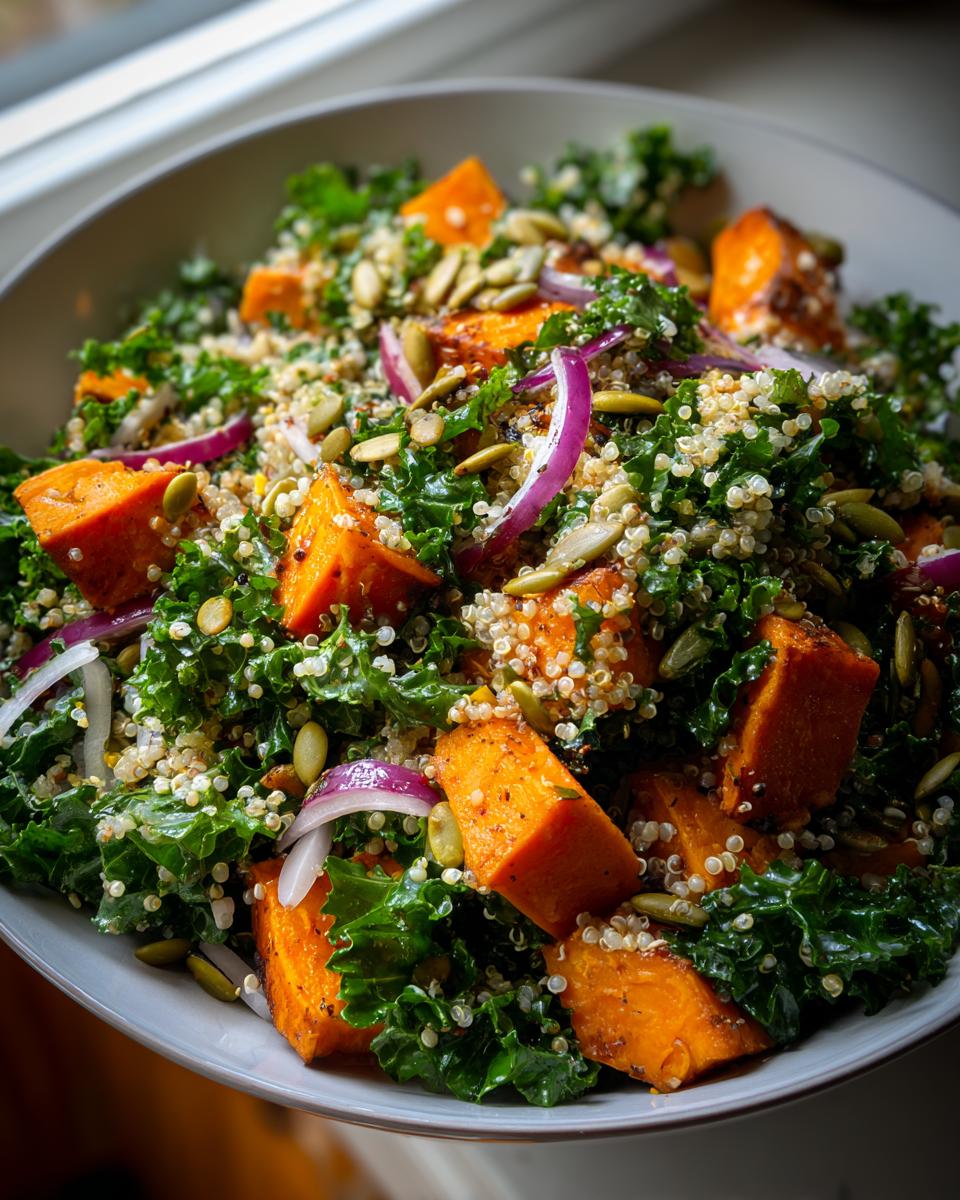 A close-up of a vibrant Sweet Potato Kale Salad with quinoa, pumpkin seeds, and red onion.
