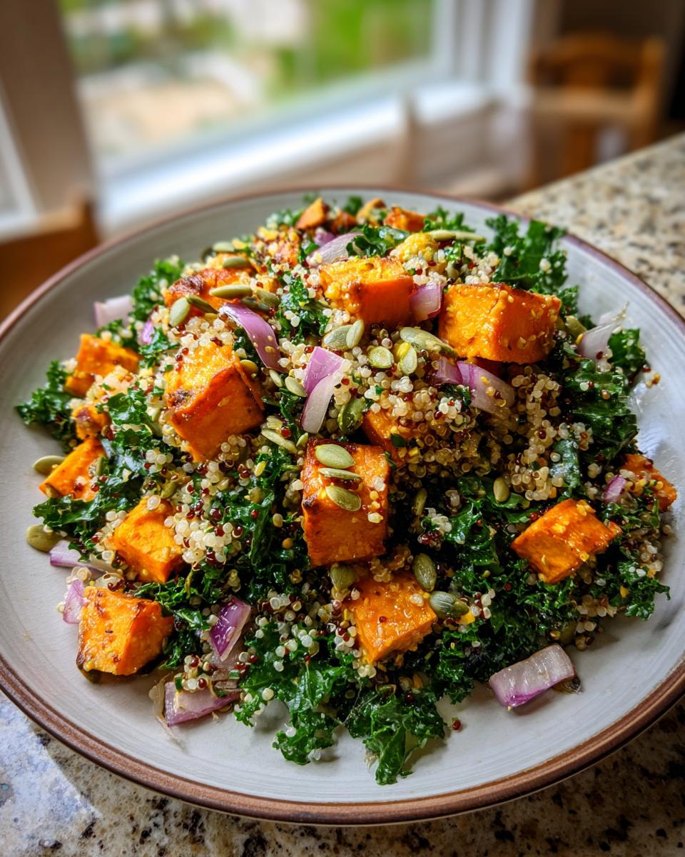 A close-up of a hearty sweet potato kale salad with quinoa, red onion, and pumpkin seeds.
